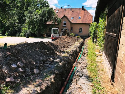 Offener Graben mit neuen Rohren neben Scheune und Mini-Bagger